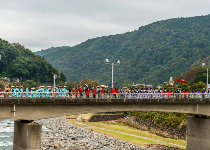 A parade crossing a bridge in Kanagawa as part of the Hakone Daimyo Gyoretsu Festival. In the background, scenic mountains.